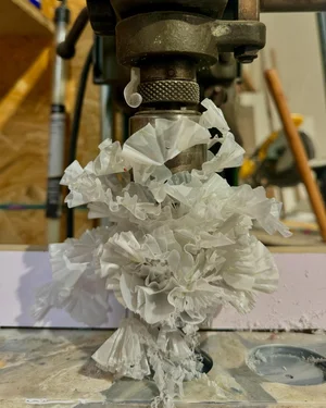 Shredded white plastic film caught on a drill-press-mounted grinding bit