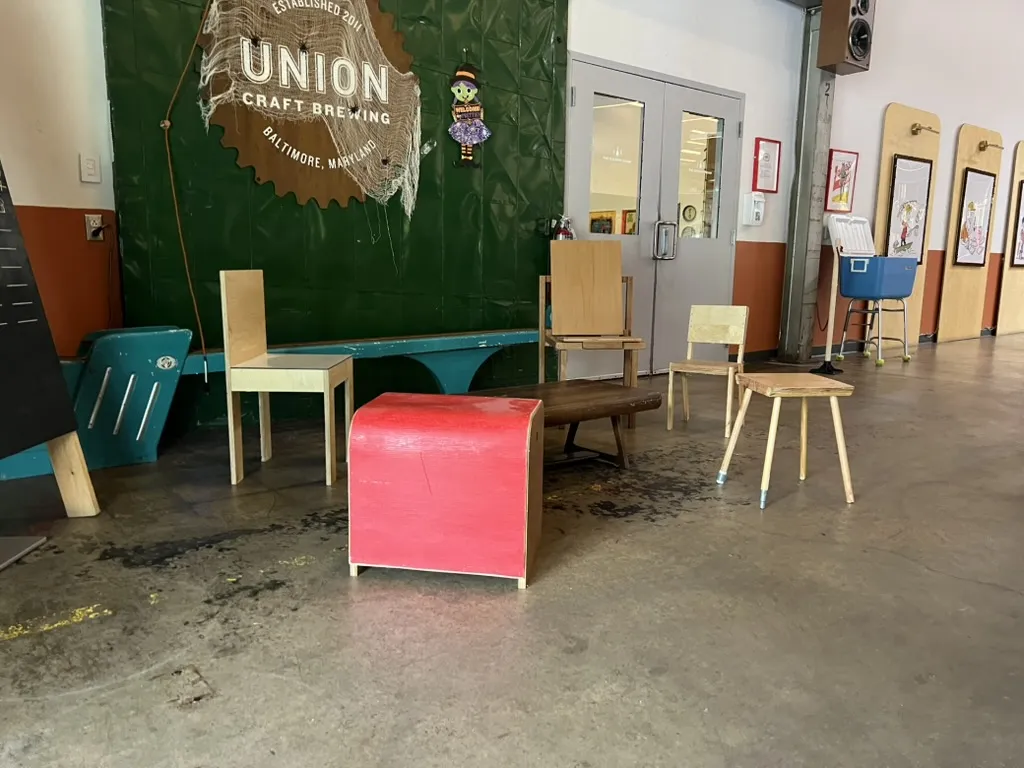 A red upholstered cube stool, a pale plywood chair and a small splay-legged stool under the Union Craft Brewing sign