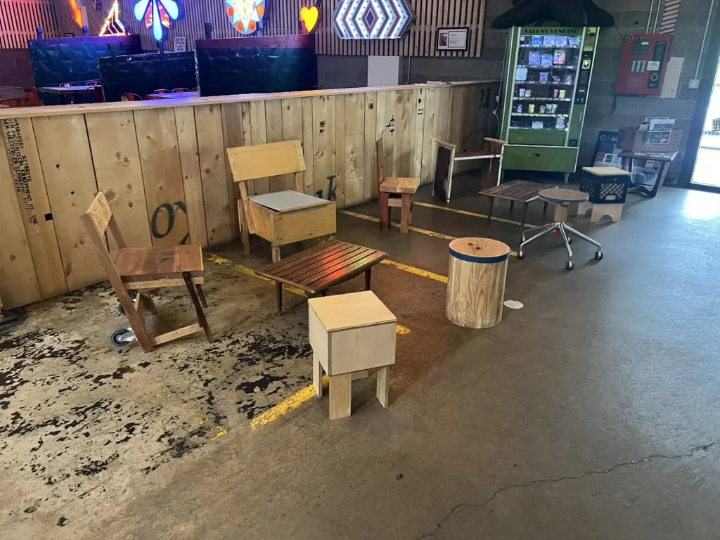 Chairs and stools grouped on a stained concrete floor under the bar’s colored lights, with a vending machine behind them