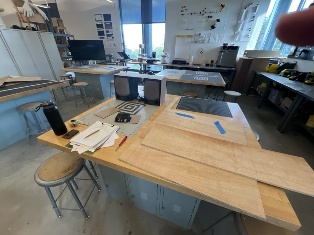 Workshop bench with plywood offcuts, a pair of salvaged bookshelf speakers, and a project notebook staged before cutting