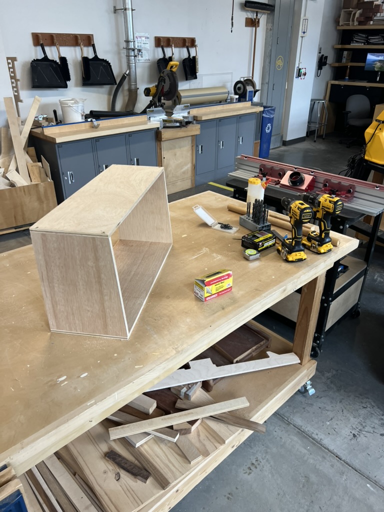 Assembled plywood enclosure sitting empty on a workbench, surrounded by drills, screws, and dowel stock