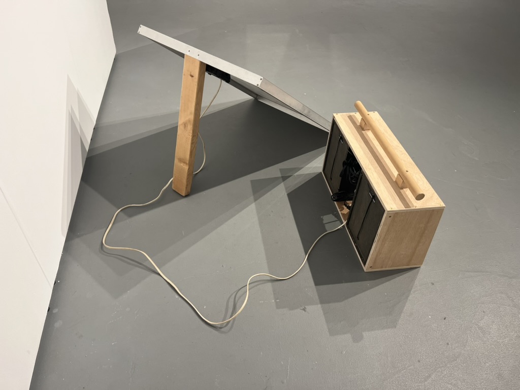 The boombox on the floor wired to a solar panel propped against the wall