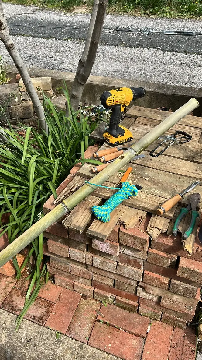 Bamboo poles, a cordless drill and paracord laid across a stack of old bricks in the yard