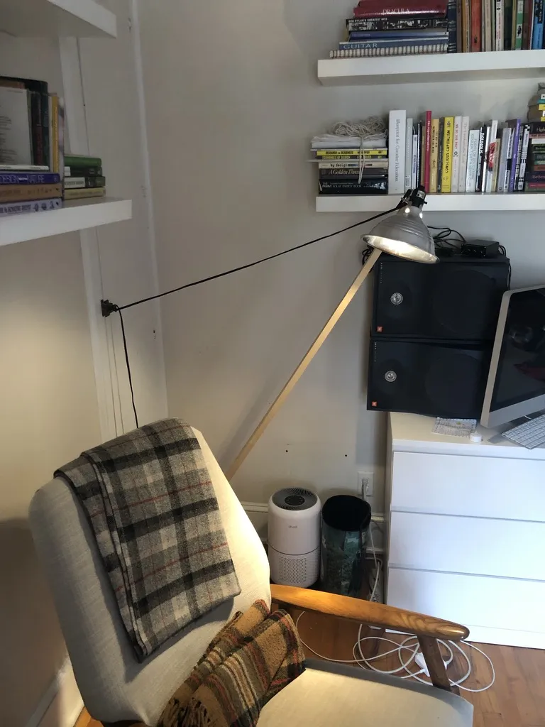 A clip-on work light at the end of a slanting wooden pole, angled over an upholstered armchair with a plaid blanket