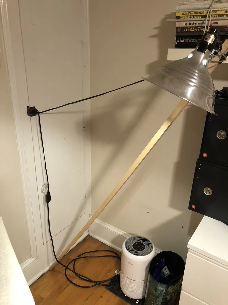 The same reading light from the side: its black cord runs taut from the lamp to a hook on the wall, holding the slanted pole in place